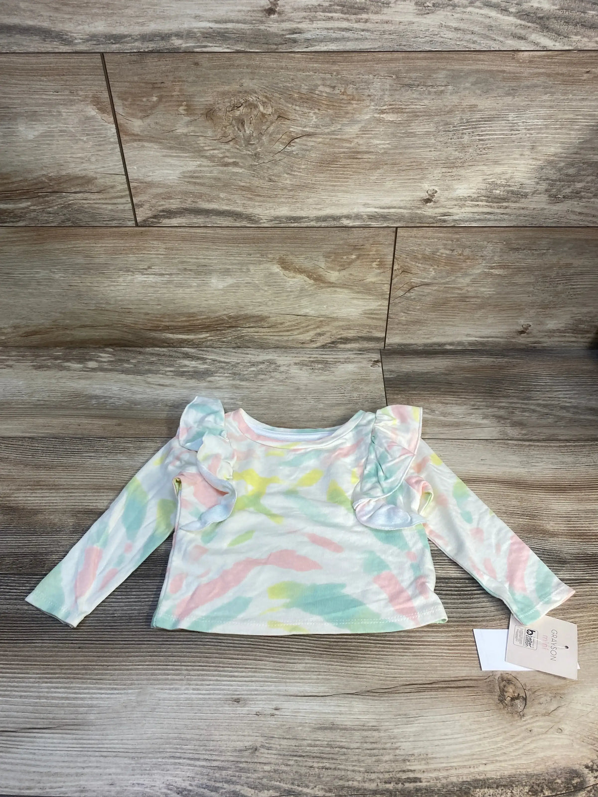 Pastel tie-dye long sleeve baby shirt with ruffle shoulders, laid on wood background