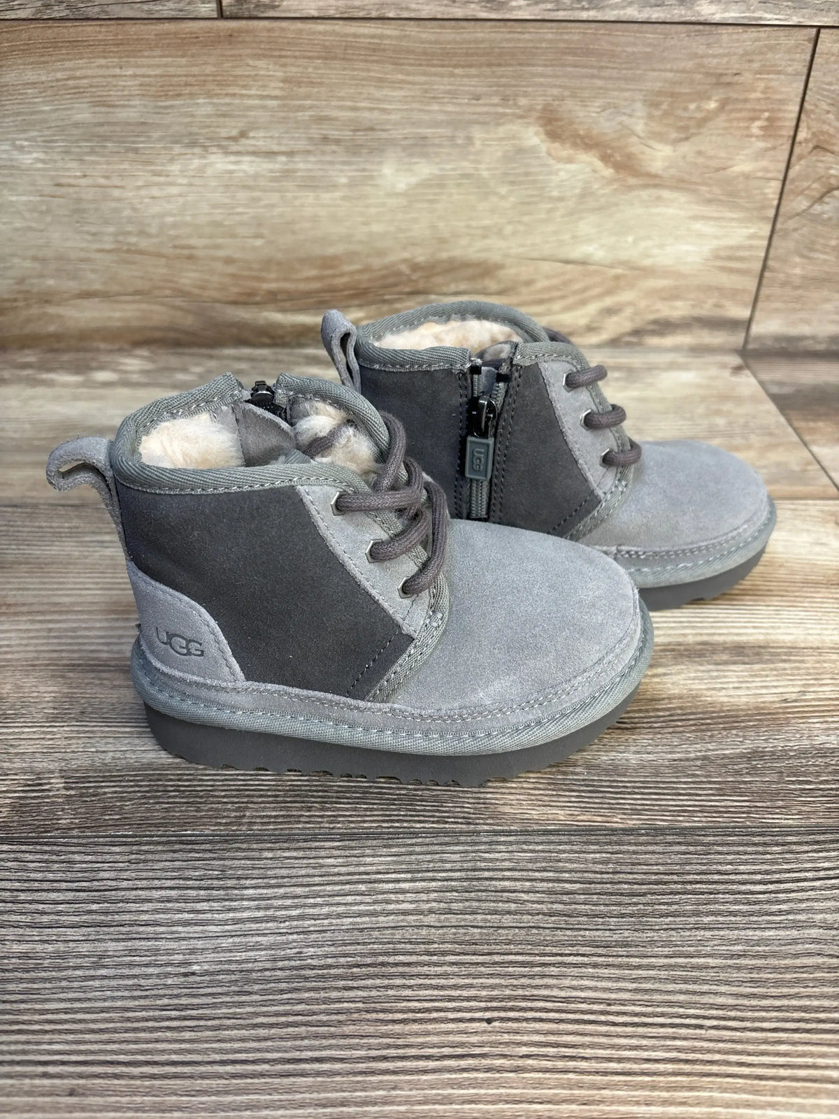 Three-quarter view of Ugg Neumel II boots in grey suede with shearling lining, side zipper and laces on wood background