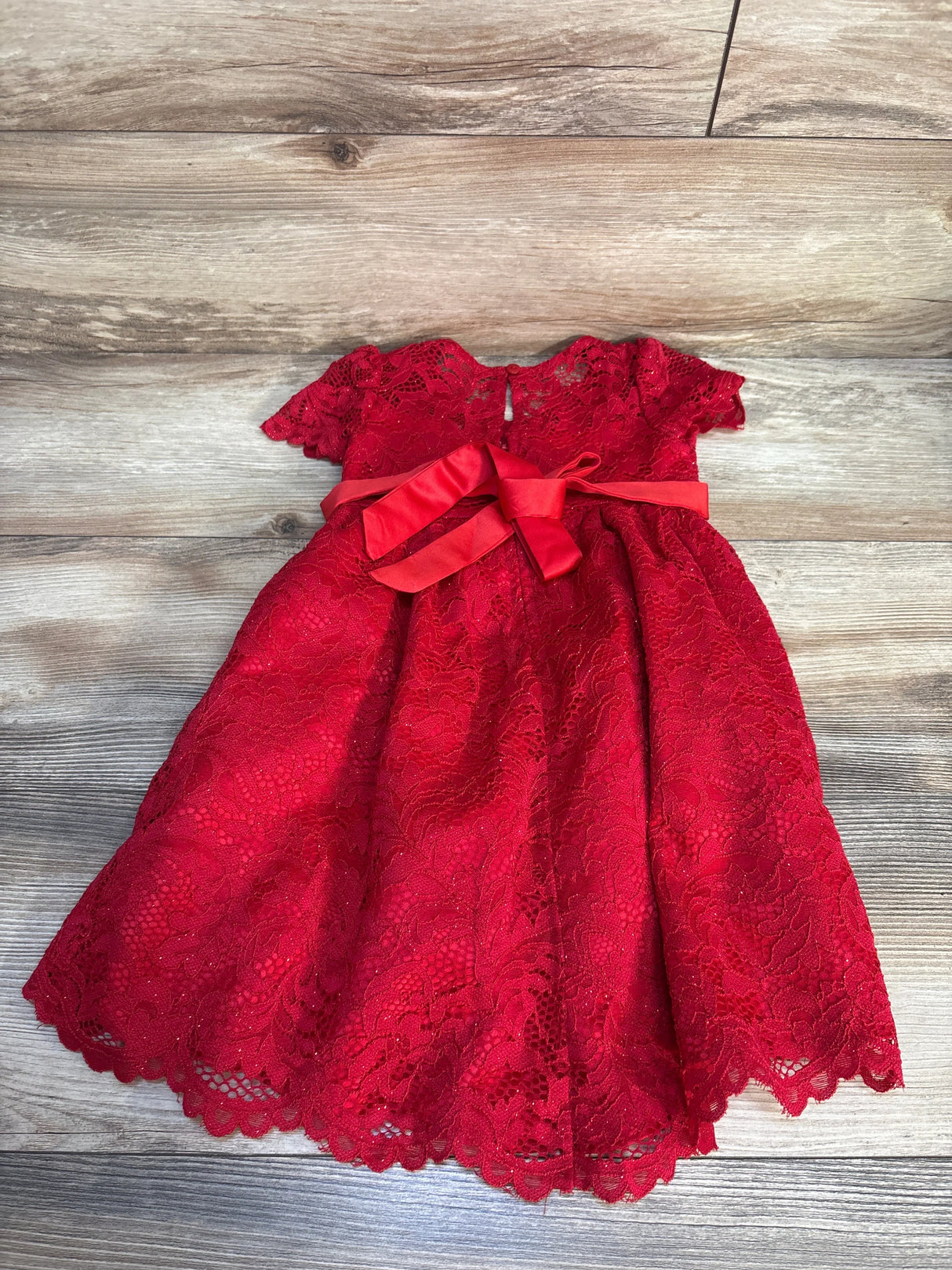 Red lace baby dress with short sleeves and a satin bow, displayed on wooden floor