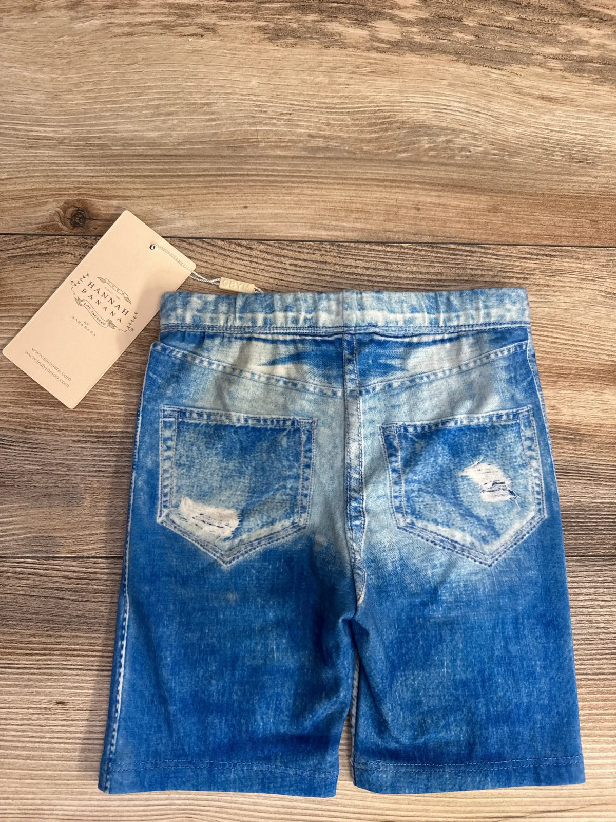 Back view of Hanna Banana faux jean toddler shorts size 4T showing distressed back pockets and faded blue wash on wood background