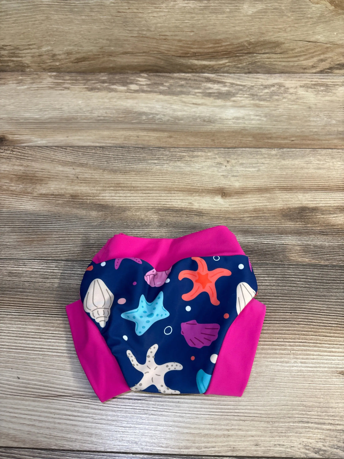Top-down view of Big Elephant reusable swim nappy showcasing navy sea creature print and bright pink waistband on wood background