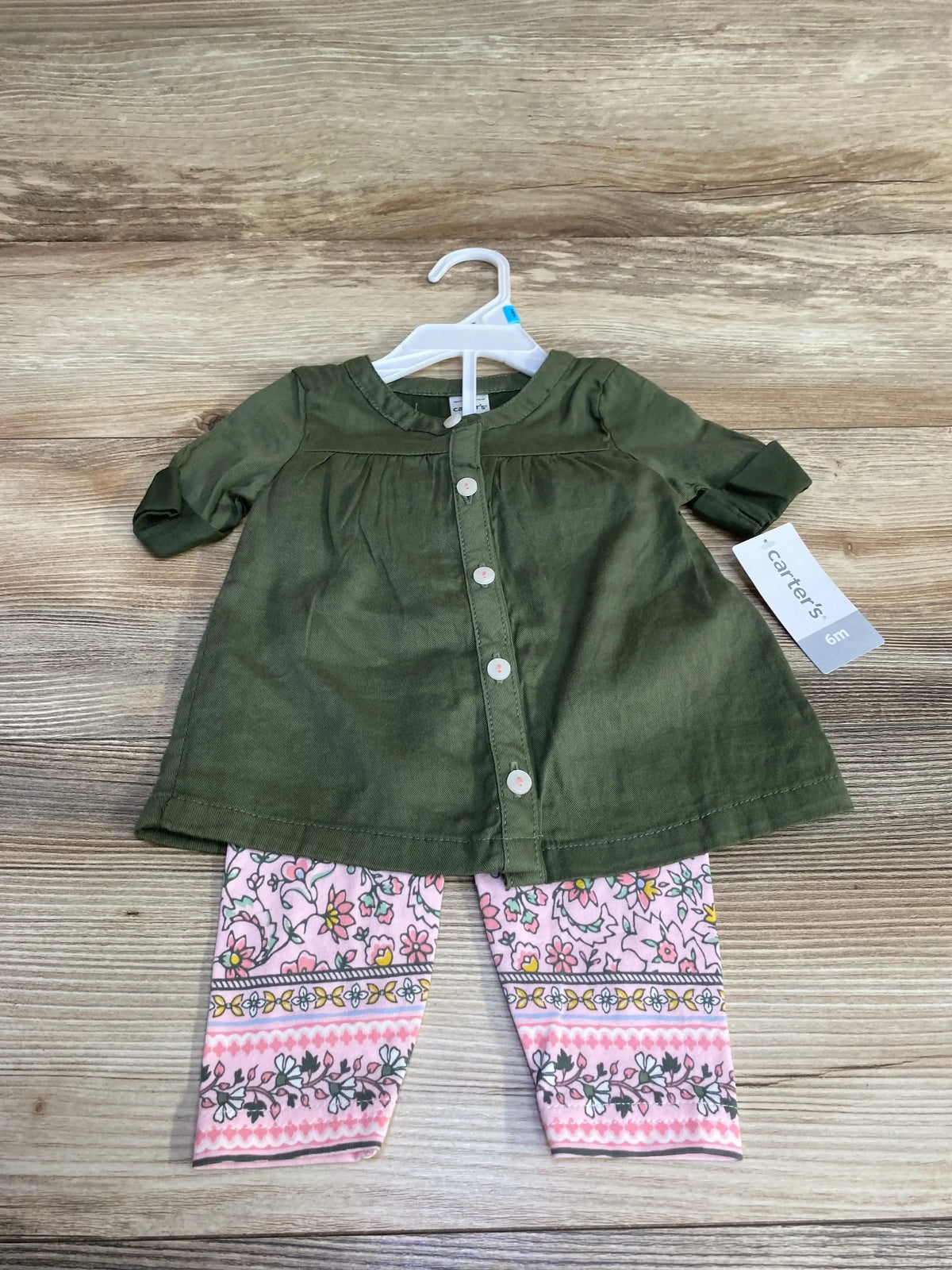 Front view of a green button-front top and pink floral leggings set on a hanger against a wood background