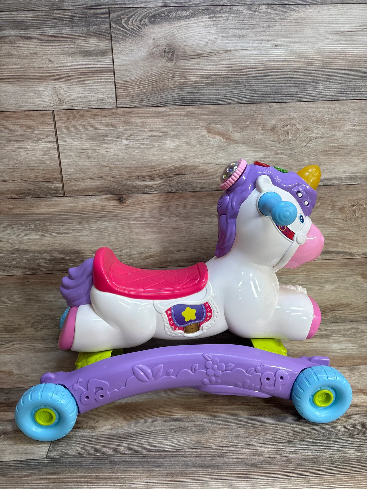 Purple unicorn ride-on toy with pink saddle, blue wheels, and musical features for toddlers