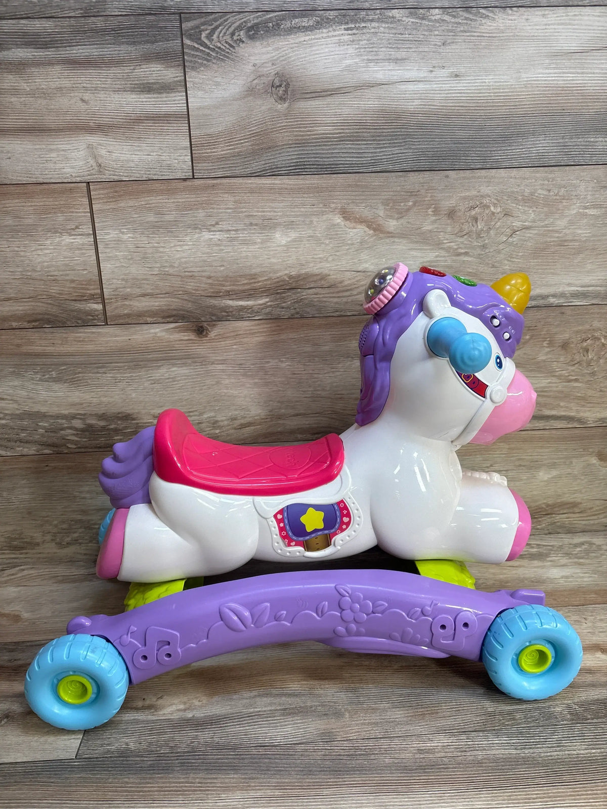 Purple unicorn ride-on toy with pink saddle, blue wheels, and musical features for toddlers