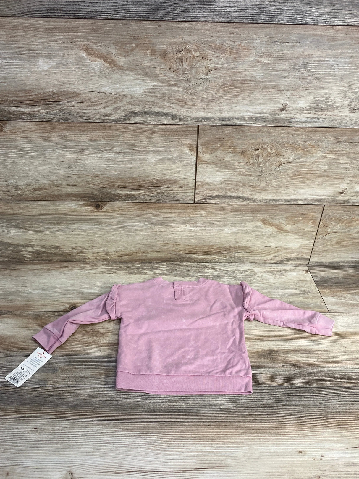 Light pink long-sleeve toddler shirt with ruffle detail, laid flat on wooden floor