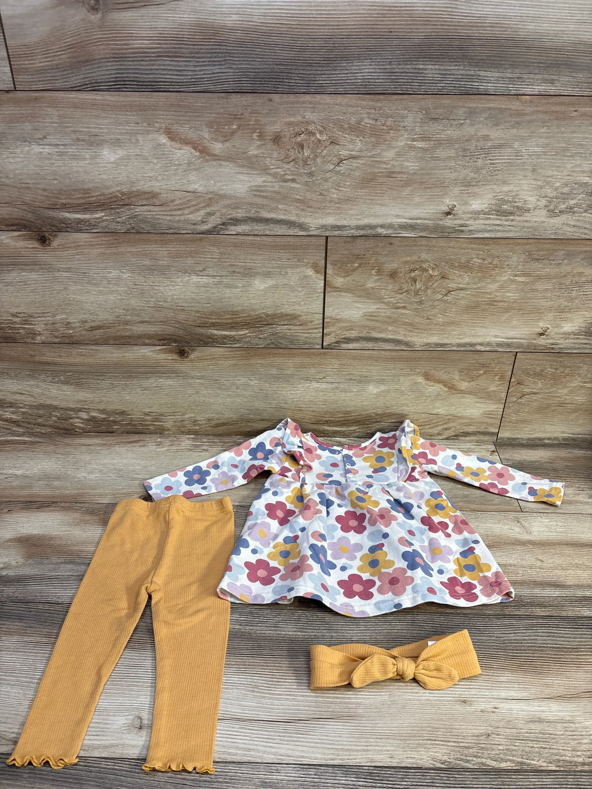Top view of Rene Rofe 3-piece floral dress, leggings, and headband set showcasing a white floral dress, mustard leggings, and bow headband on wood