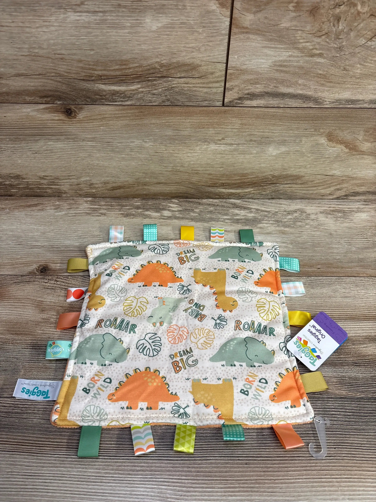 Dinosaur print baby sensory tag blanket with colorful ribbon loops on wood background