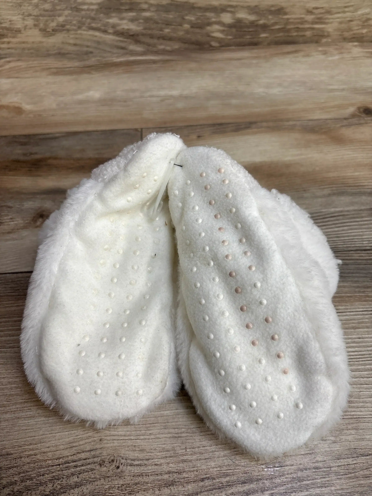 Top view of white Art Class baby slippers size S/M showing non-slip dotted soles on wooden floor