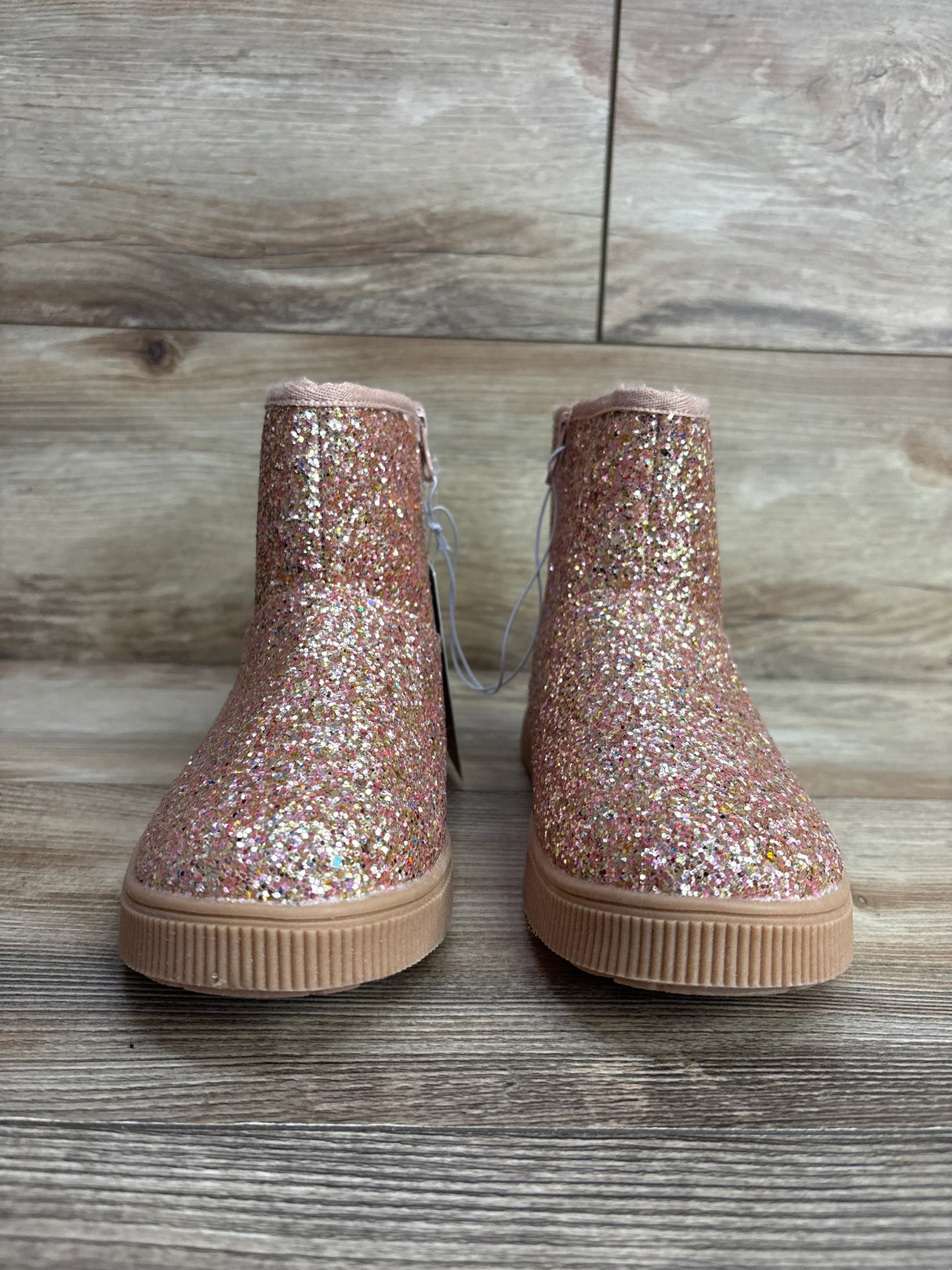 Pink glitter ankle boots for kids with rubber soles on a wooden floor