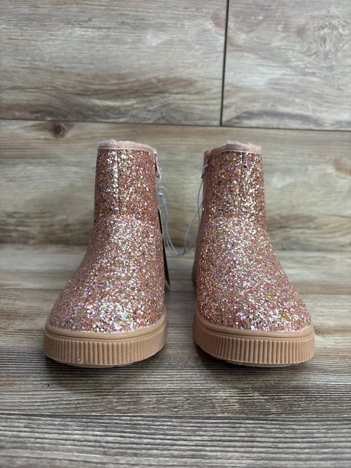 Pink glitter ankle boots for kids with rubber soles on a wooden floor
