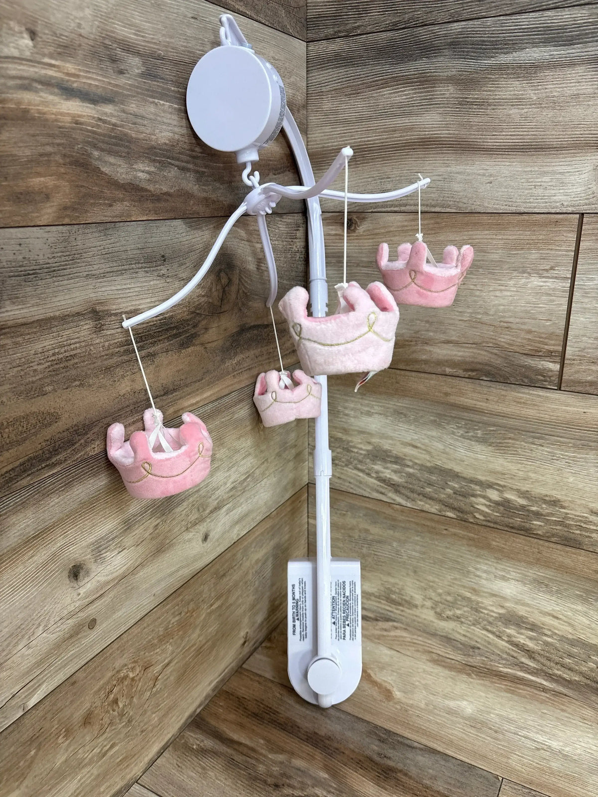 White baby crib mobile with four hanging soft plush pink crown toys on wood background