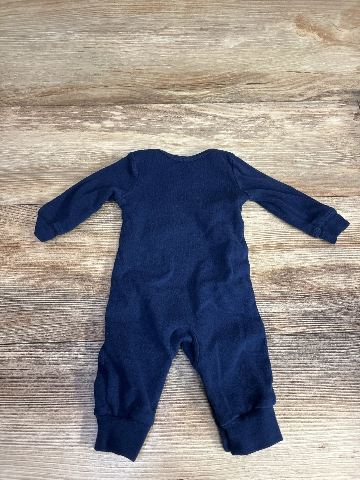 Navy blue baby onesie with long sleeves and legs, laid flat on wood floor
