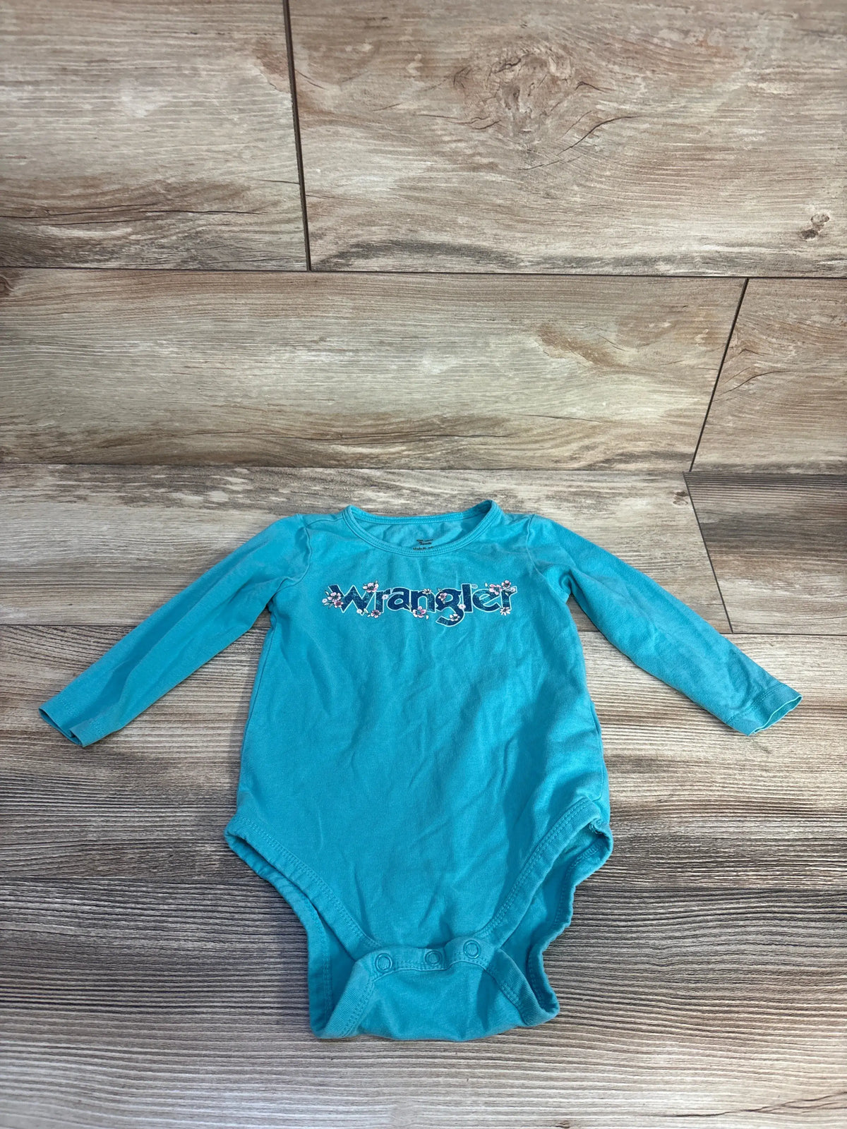 Front view of Wrangler teal long sleeve bodysuit showcasing Wrangler graphic and snap closures on a wood-look floor