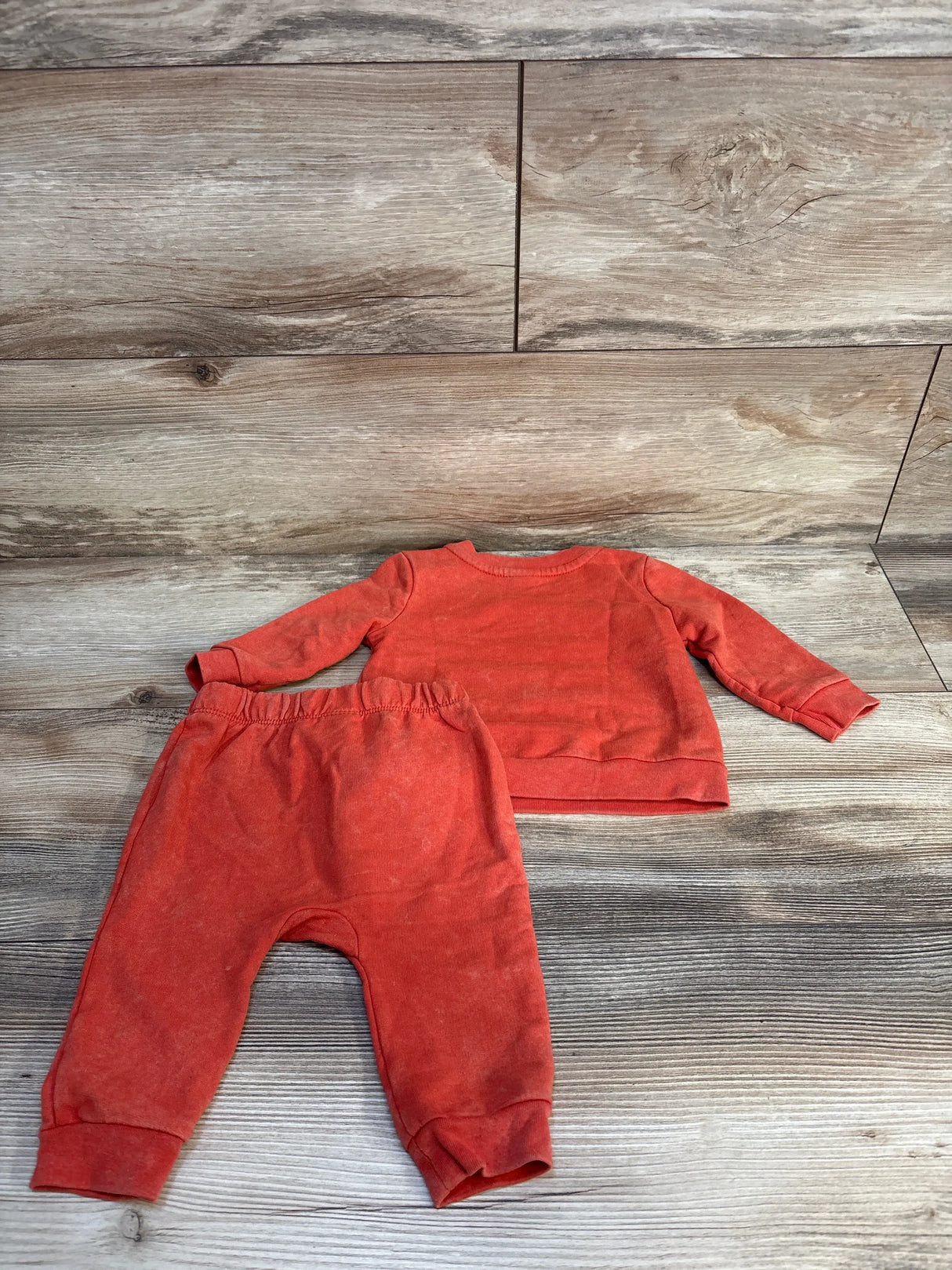 Back view of Cat and Jack 2pc Oh So Loveable Sweatshirt and Bottoms Set Orange sz 3-6m showcasing washed orange sweatshirt and joggers on wood plank floor