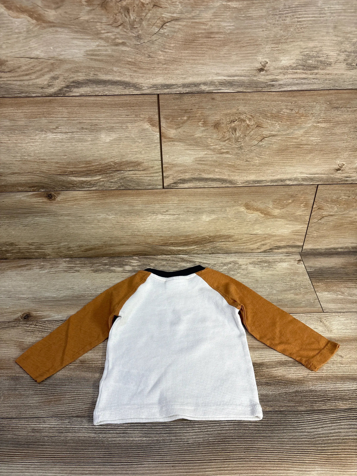 Front view of Timberland waffle knit shirt, size 12 months, showcasing waffle knit texture and tan long sleeves on wood floor