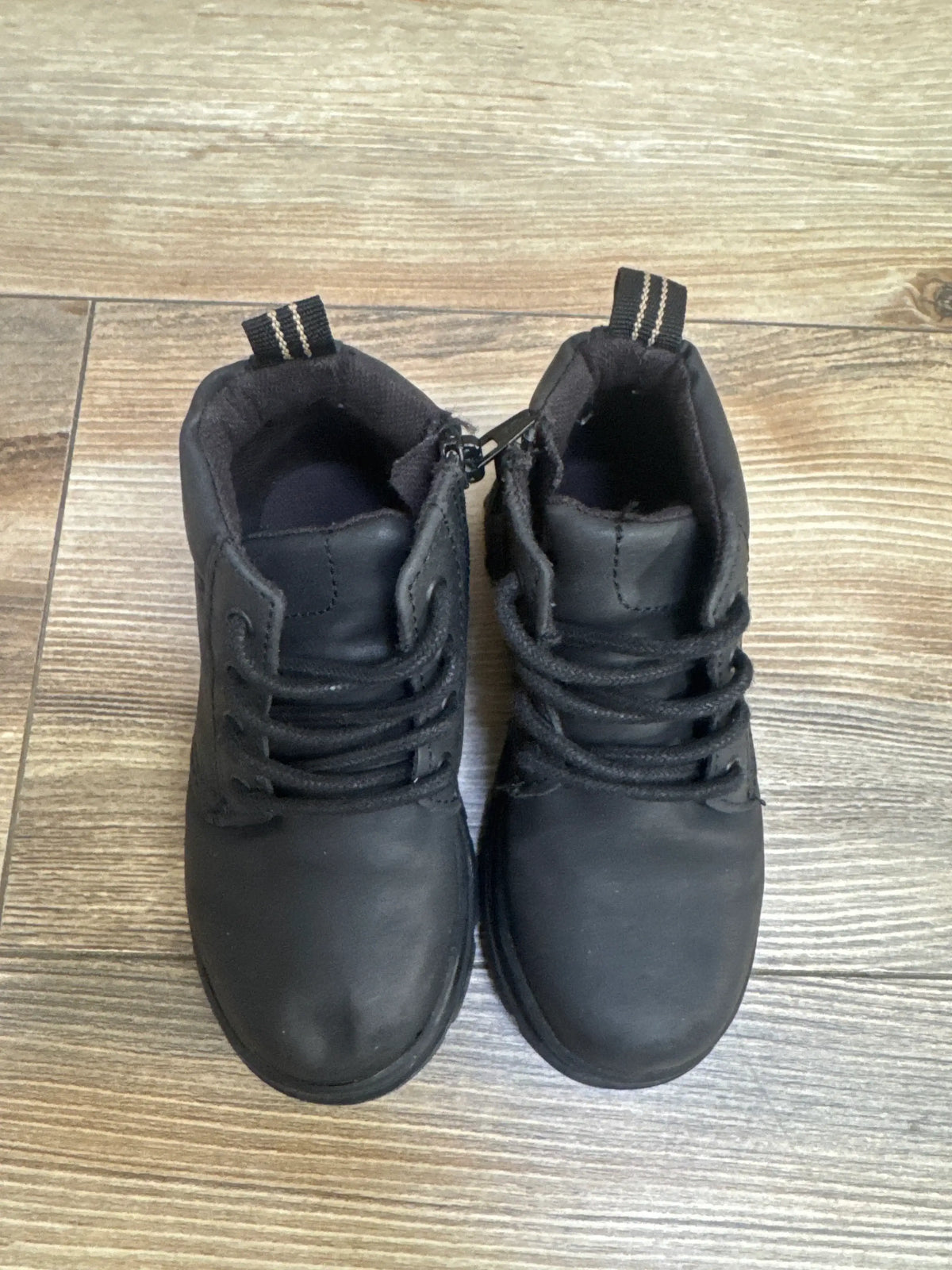 Top-down view of black Zara boys ankle boots size 7C showing lace-up front, side zipper, and heel pull tabs on wood floor