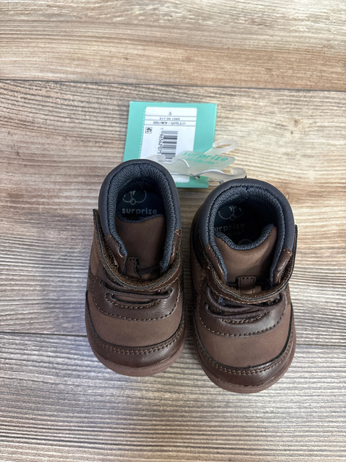 Pair of brown baby shoes with black lining on wooden surface, size 3, surprise brand