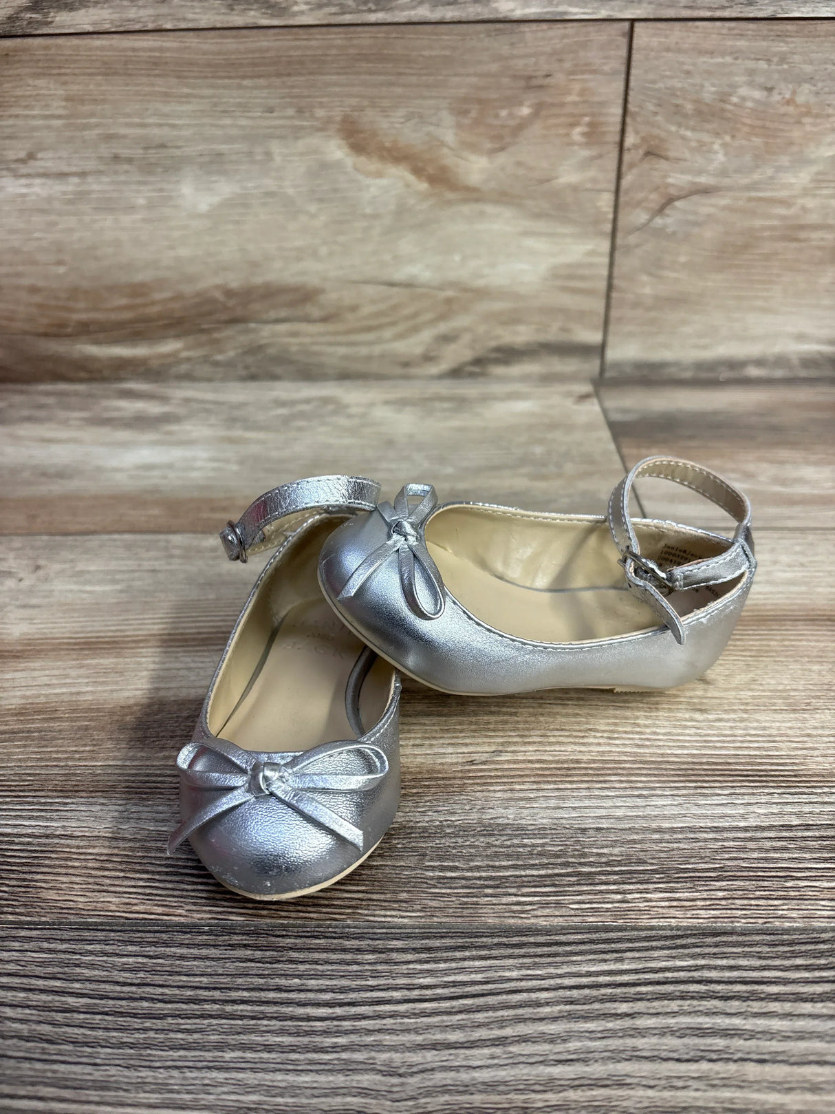 Silver toddler girl shoes with ankle straps and front bows on wooden floor