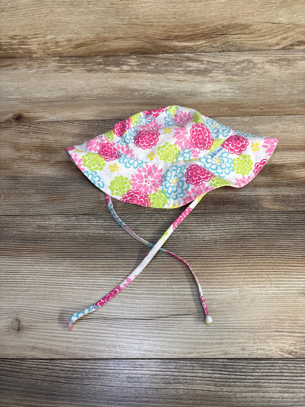 Top view of iPlay by Green Sprouts white swim bucket hat with colorful floral print and chin strap on wood grain