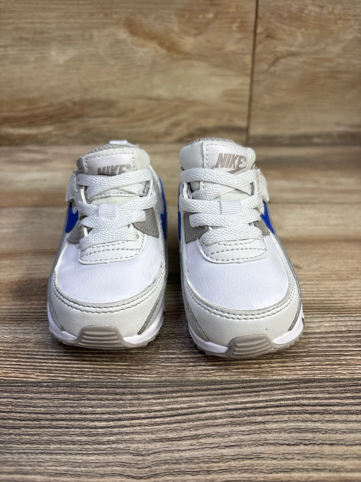 Front view of Nike Air Max 90 EasyOn TD toddler sneakers size 5C showing white uppers, blue Swoosh and College Grey accents on a wood floor