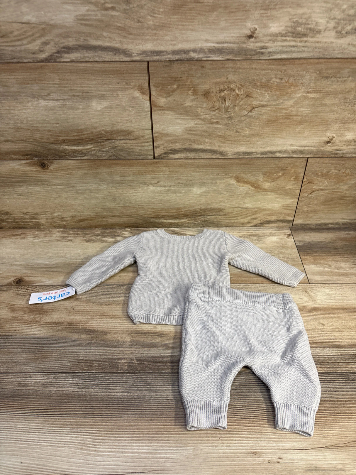 Top-down view of Just One You grey 2-piece knit baby sweater and pants showcasing ribbed cuffs and elastic waist on wood background, 3 months