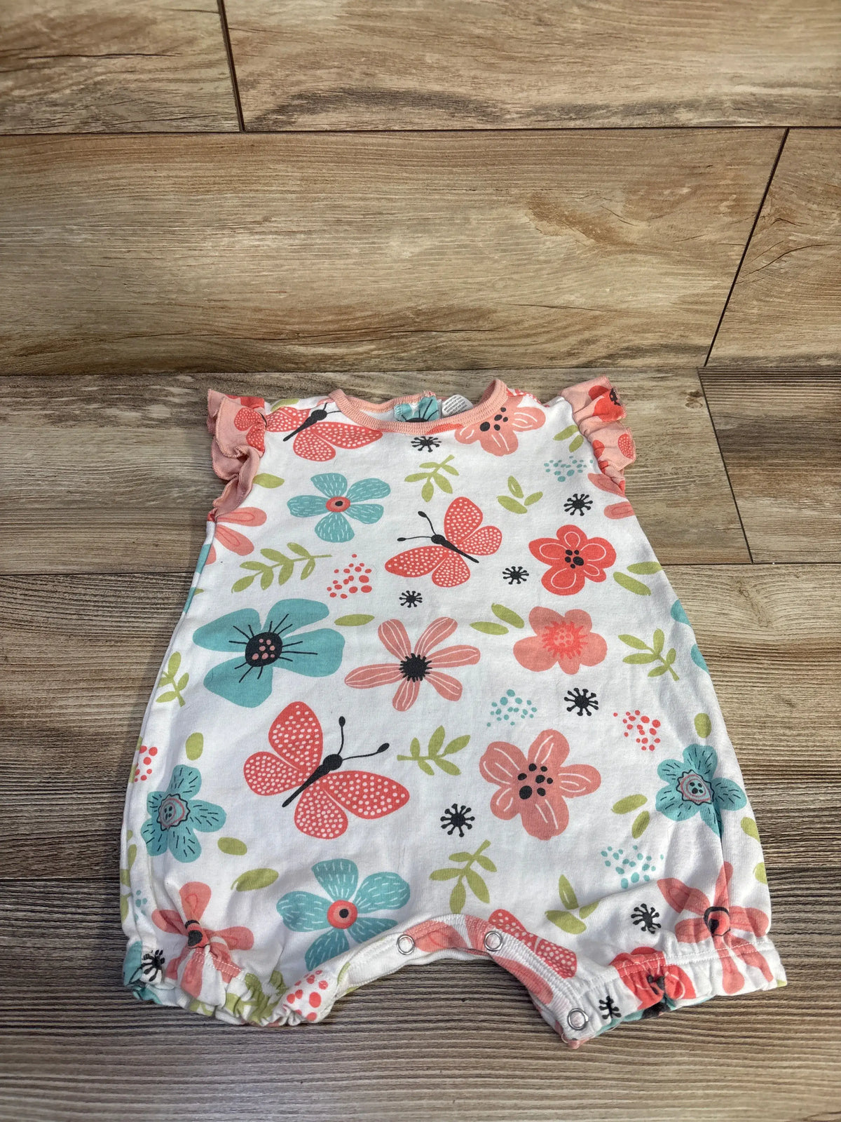 Front view of Tesa Babe butterfly shortie romper showcasing pink ruffle trim, floral print, and snap closures on wood floor