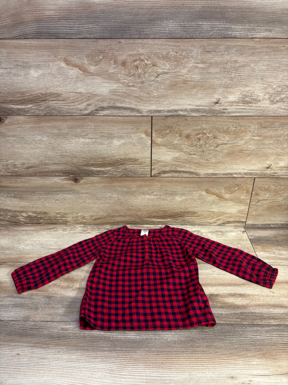 Red and black buffalo plaid Henley shirt for toddlers laid flat on a wood background.