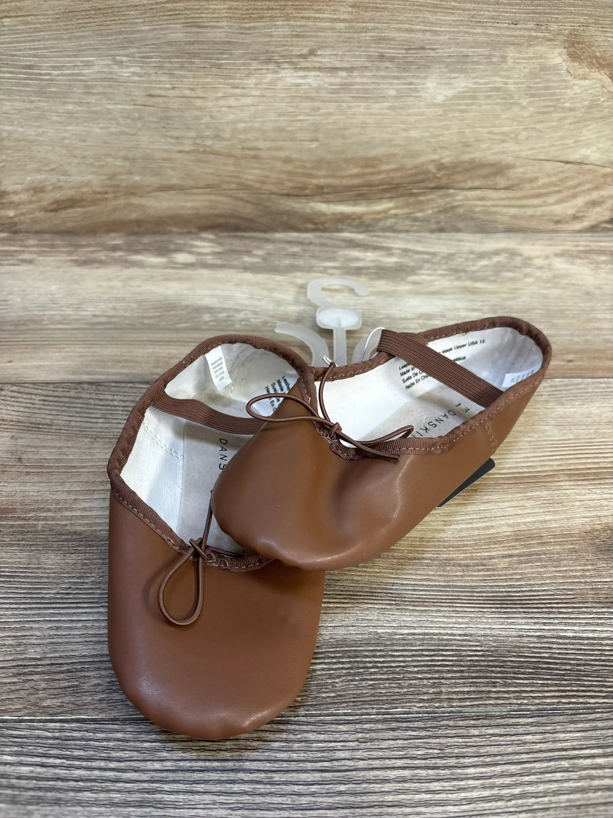 Brown toddler ballet flats with elastic straps on a wood background