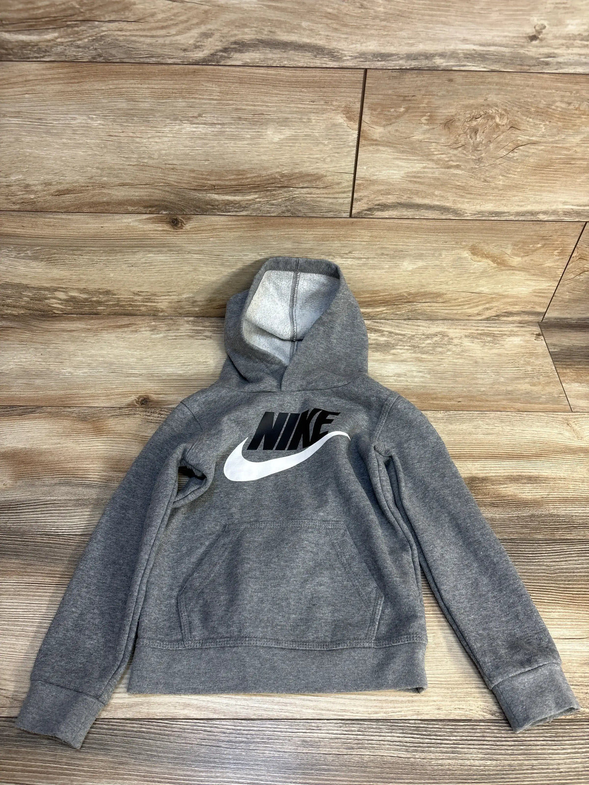 Gray Nike kids hoodie with black logo, laid flat on wood floor for resale