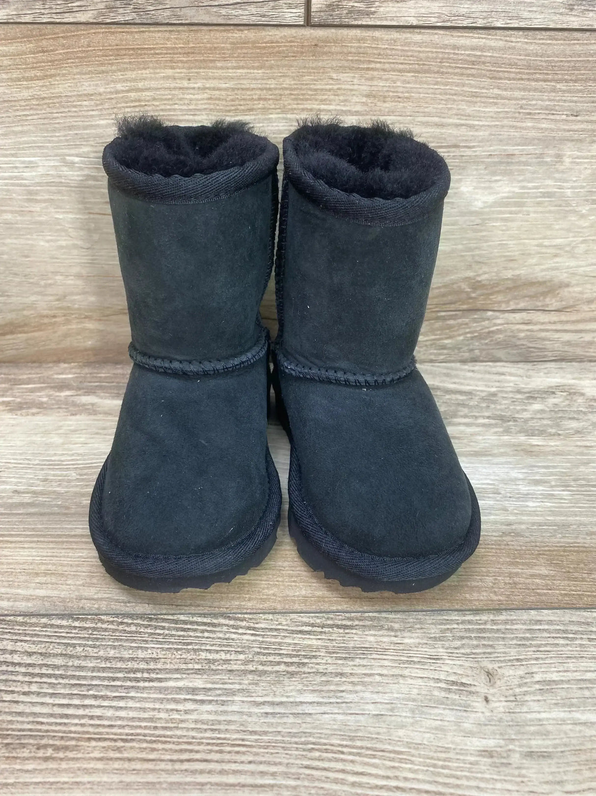 Front view of UGG Toddlers' Classic II boots showing plush shearling lining and black suede on light wood background