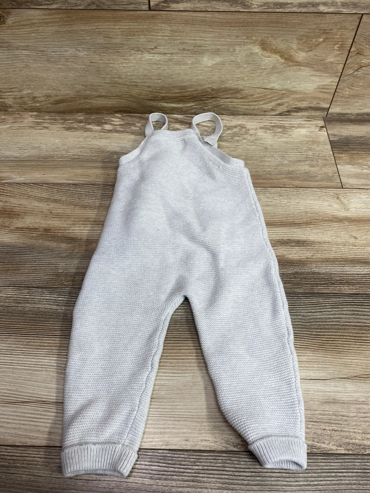 Front view of Little Planet gray knit overalls, size 18 months, showcasing shoulder straps and ribbed cuffs on a wood floor