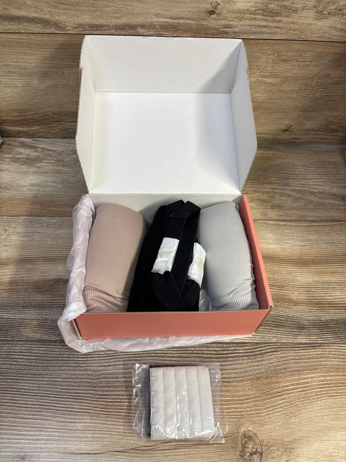 Top view of Hofish nursing maternity bras 3-pack (beige, black, gray) in box showing rolled cups and included hook extender on wood surface