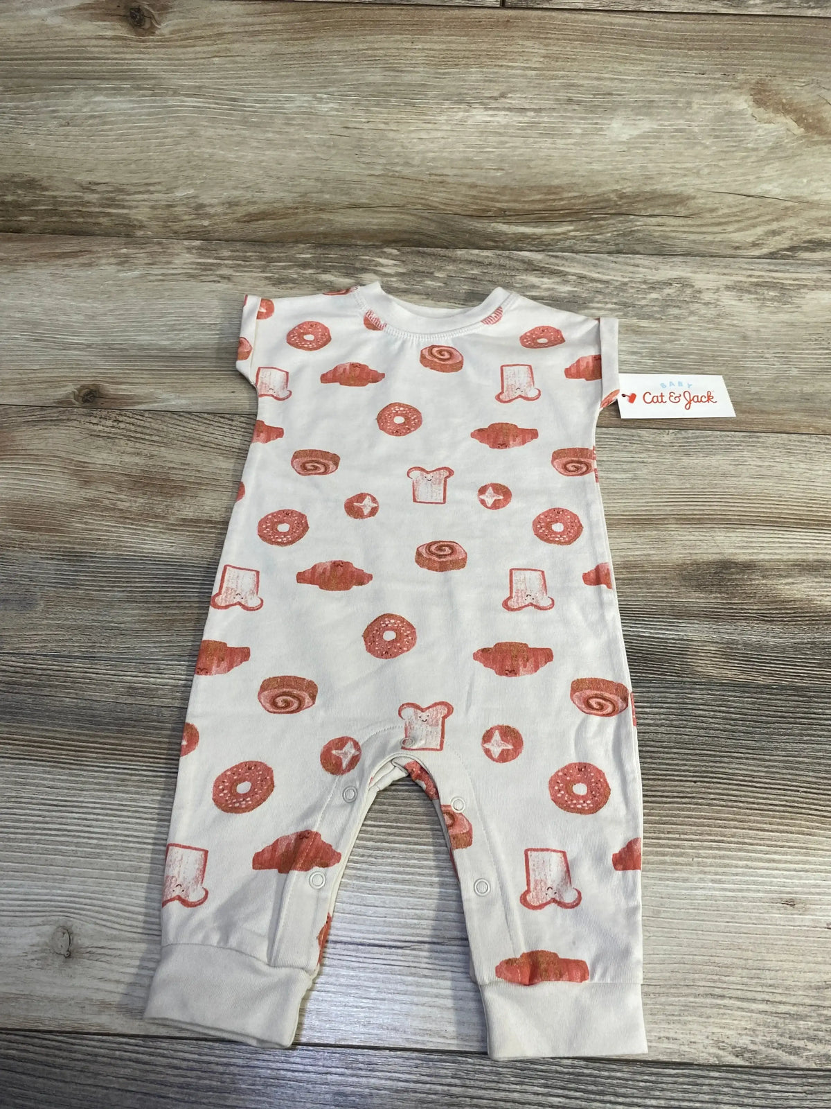 Flat-lay of beige baby coverall with orange pastry print and snap crotch on wood background, size 0-3 months