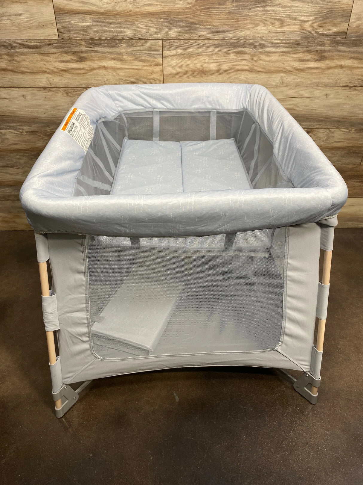 Front view of Maxi-Cosi Swift Playard in Classic Slate showing mesh sides, padded top rail, and wood-paneled wall background