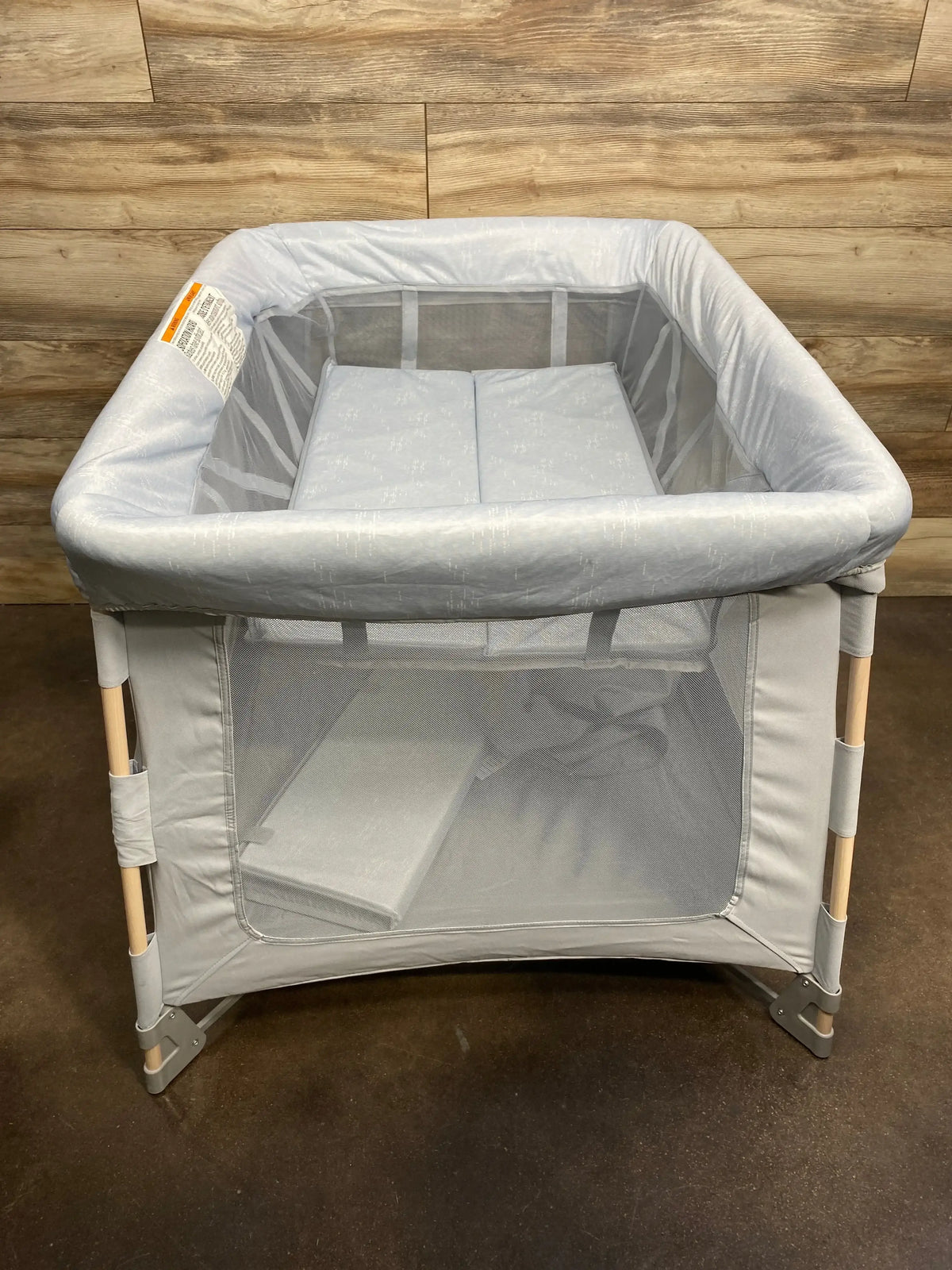 Front view of Maxi-Cosi Swift Playard in Classic Slate showing mesh sides, padded top rail, and wood-paneled wall background