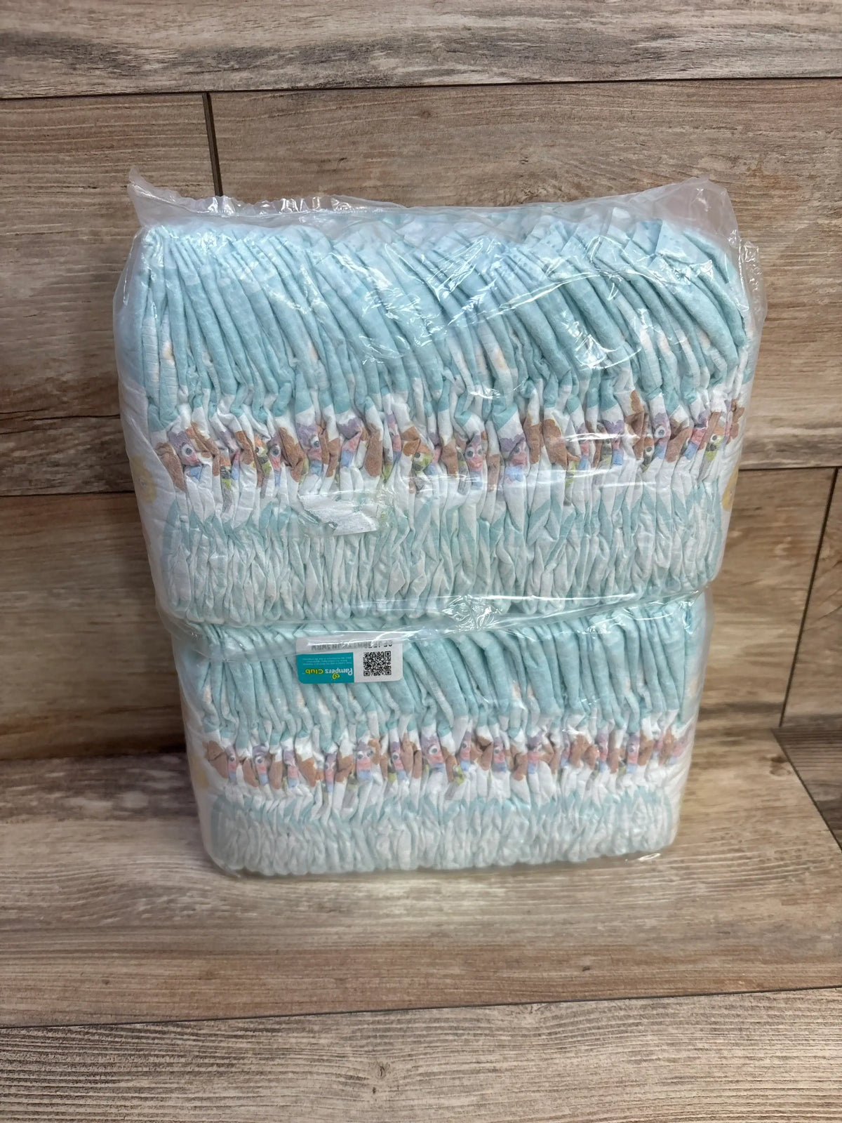 Front view of NEW Sleeve of Pampers Diapers 60ct Size 1 in sealed mint green plastic packaging on wood plank floor