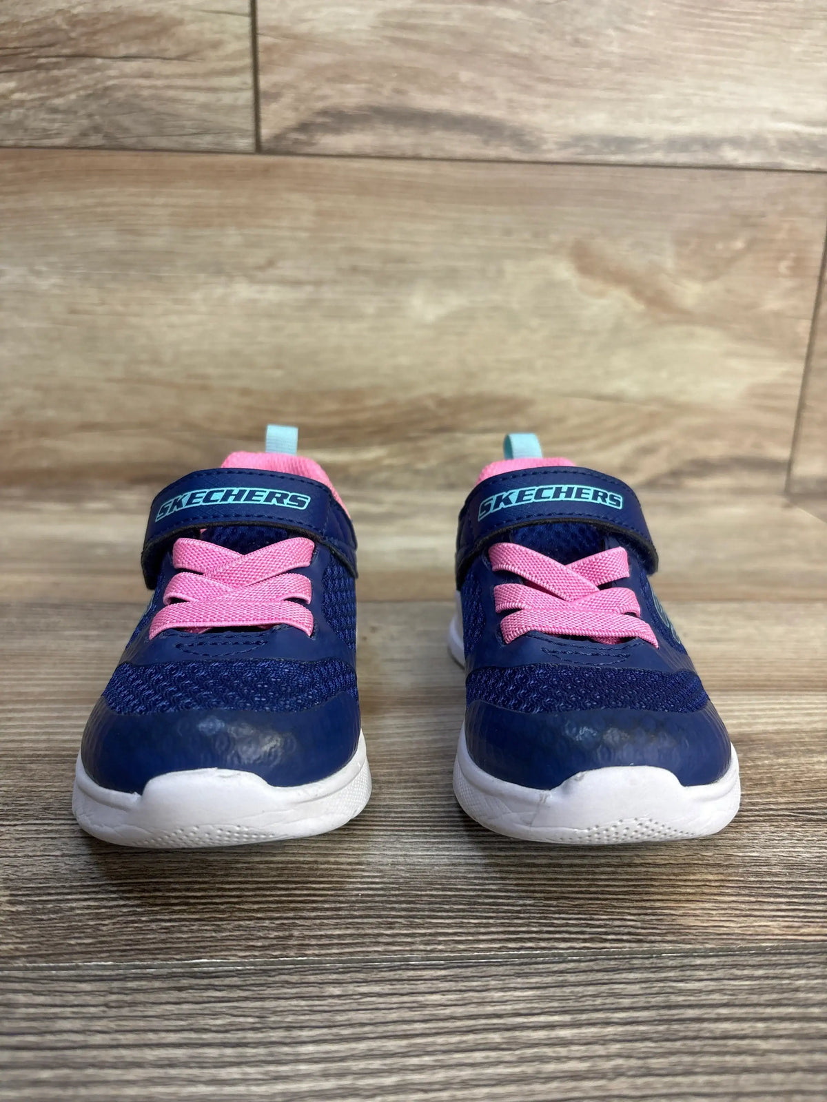 Navy blue Skechers toddler sneakers with pink laces and white soles on wood floor