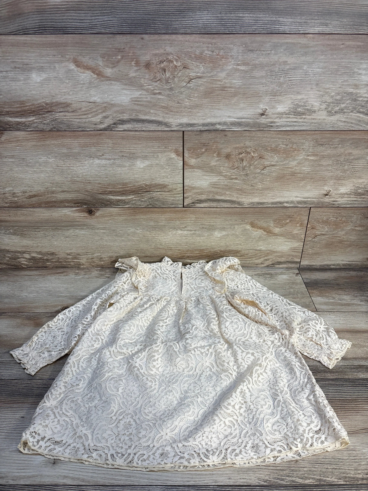 Ivory lace long sleeve baby dress with ruffle shoulders on wood background