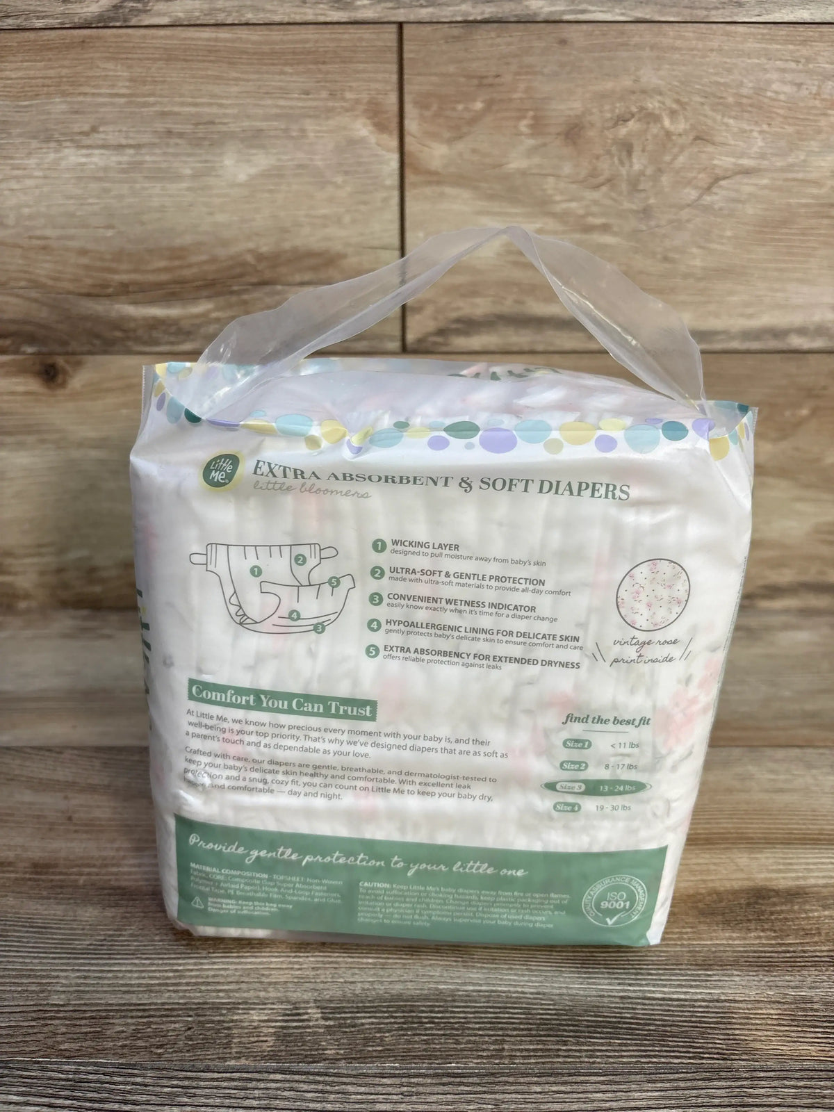 Rear view of Little Me diaper package Size 3 22 ct showing ‘Extra Absorbent & Soft Diapers’, features list and plastic handle on wood background