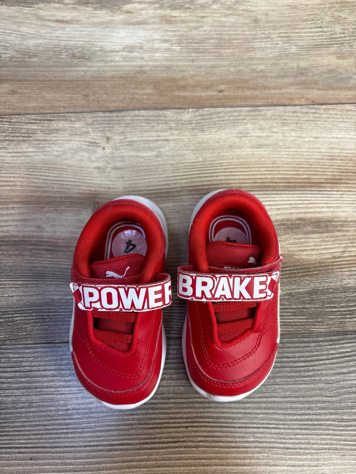 Top view of red Puma x Scuderia Ferrari Kart Cat III sneakers with POWER BRAKE hook and loop straps on wood grain