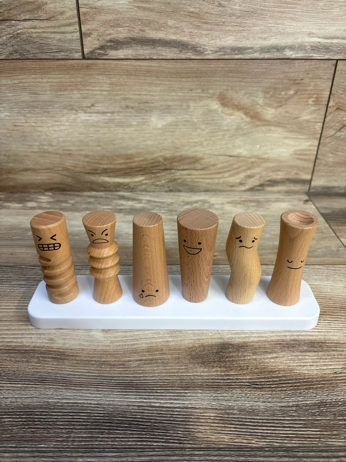Front view of Lovevery Wooden Emotion Dolls: six wooden peg figures with different facial expressions on a white base