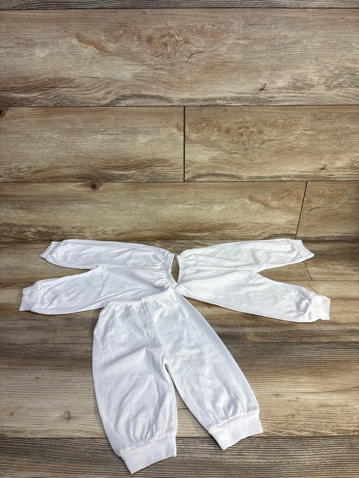 White baby onesie with long sleeves and pants, laid flat on wood floor for kids clothing resale