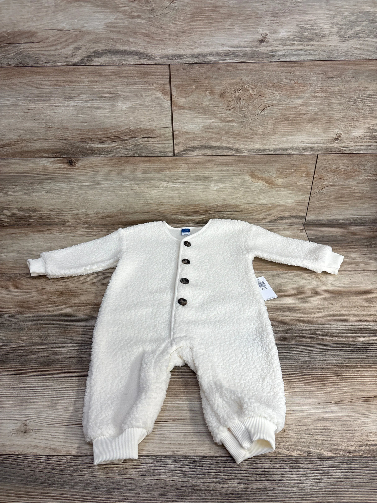 White fleece baby romper with front buttons on wood background, cozy infant clothing