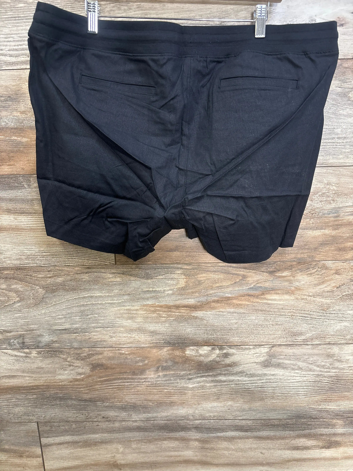 Rear view of black Gap maternity linen-blend shorts showcasing back welt pockets and elasticized waistband on wood flooring