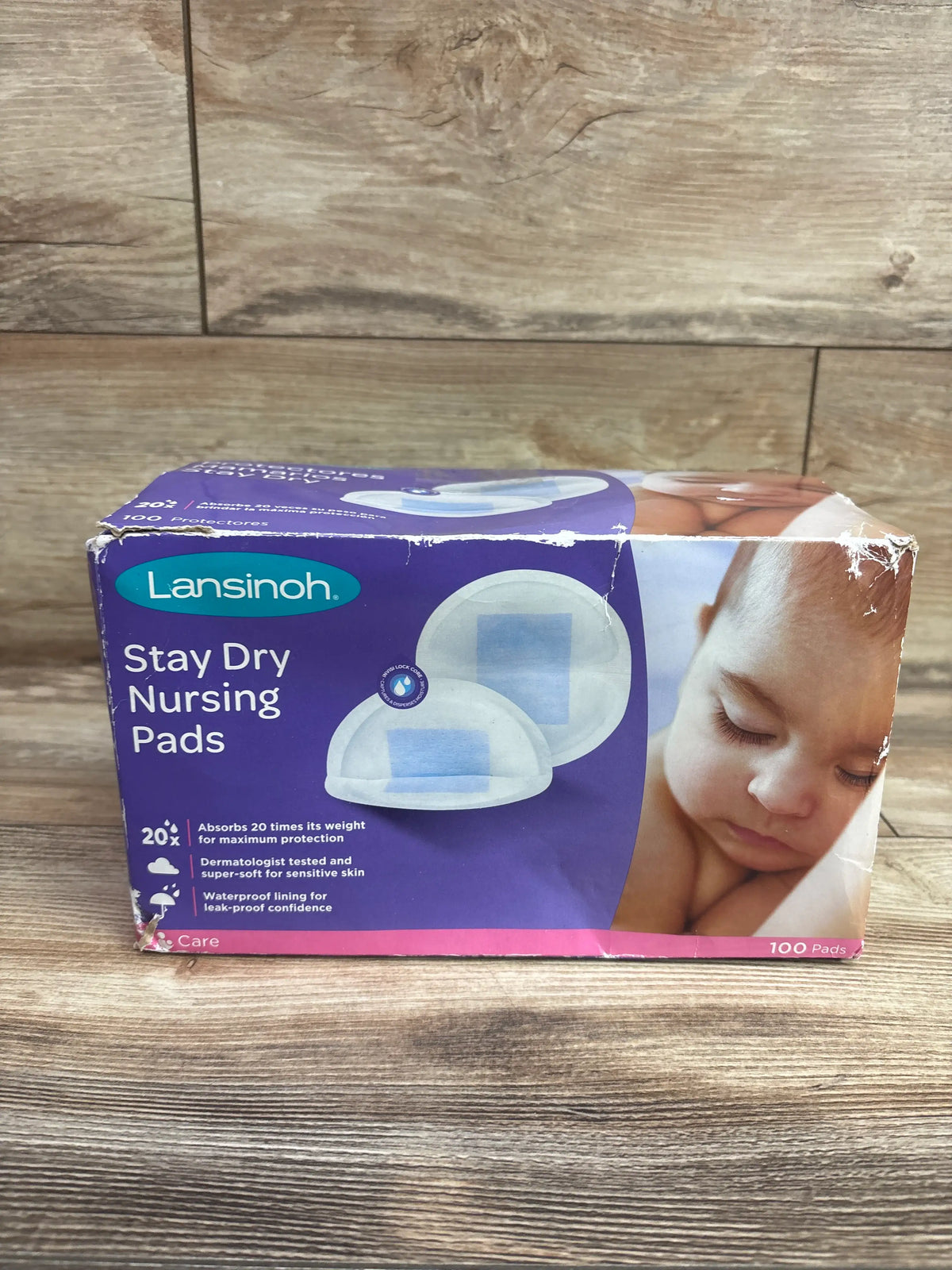 Front view of Lansinoh Stay Dry Nursing Pads package showcasing 100 pads and waterproof lining on a wood surface