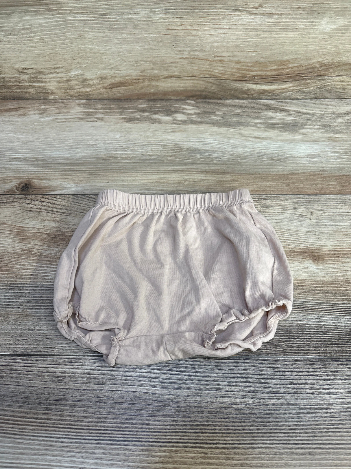 Flat lay of H&M beige cotton jersey baby bloomers showing elastic waistband and ruffled leg openings on wood background
