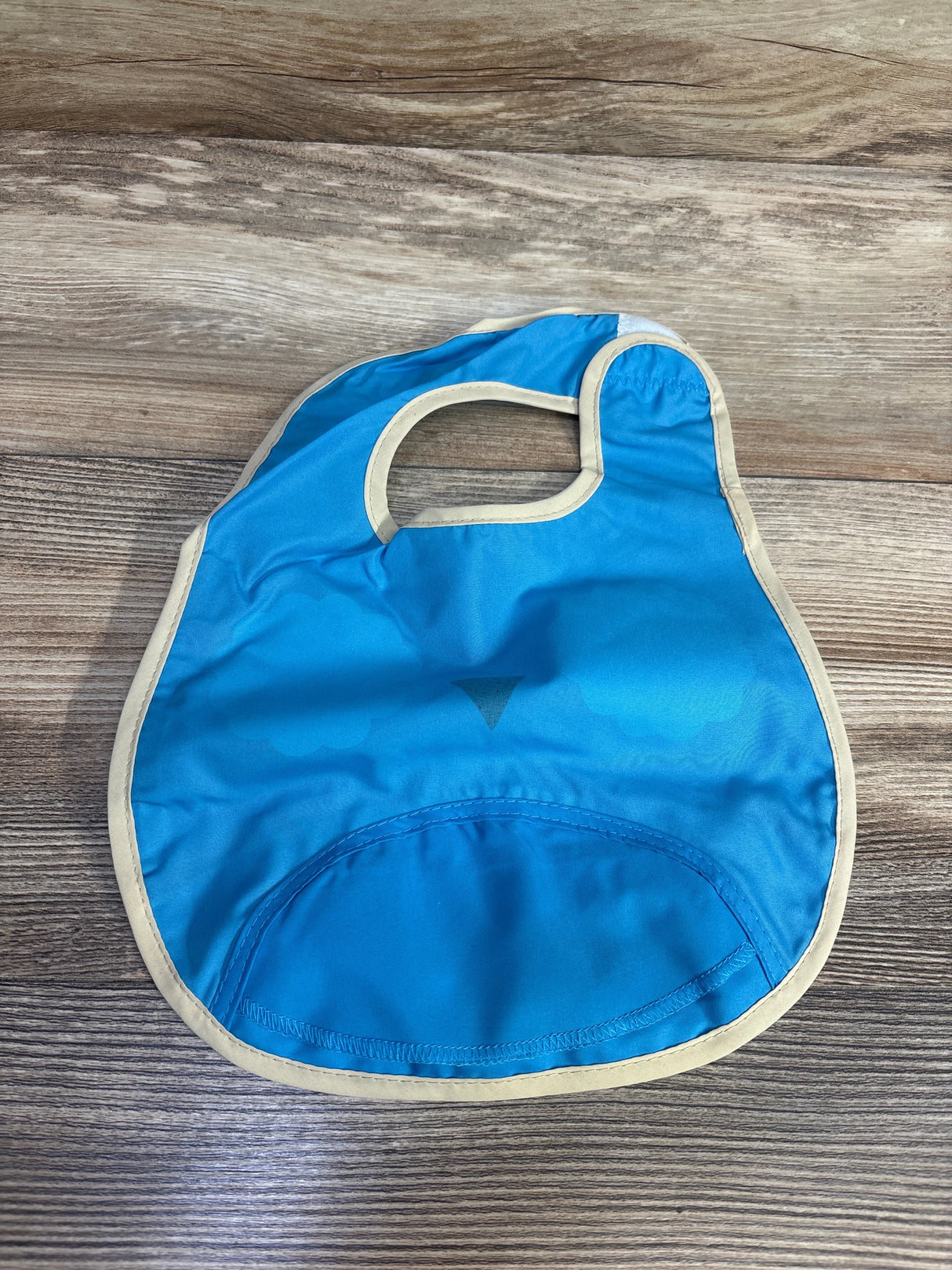 Top-down view of Skip Hop Zoo Tuck-Away Owl bib showcasing front catch pocket and beige trim with wood tabletop background