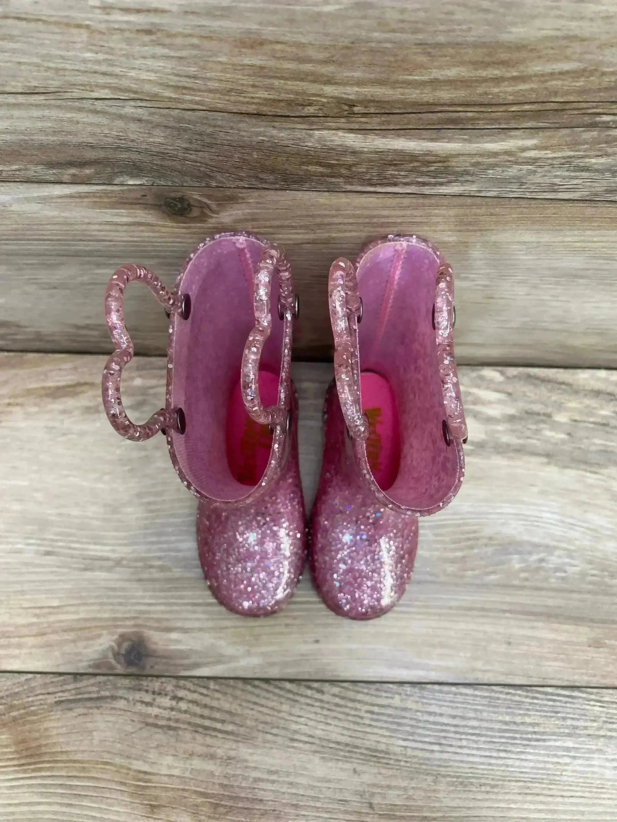 Top-down view of toddler pink glitter Western Chief light-up rain boots with pull handles on wood background
