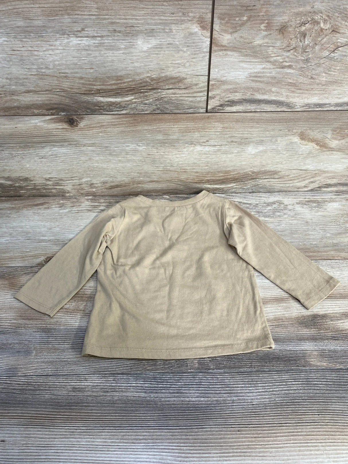 Back view of beige long-sleeve toddler shirt (12 months) showing plain back on wood plank background