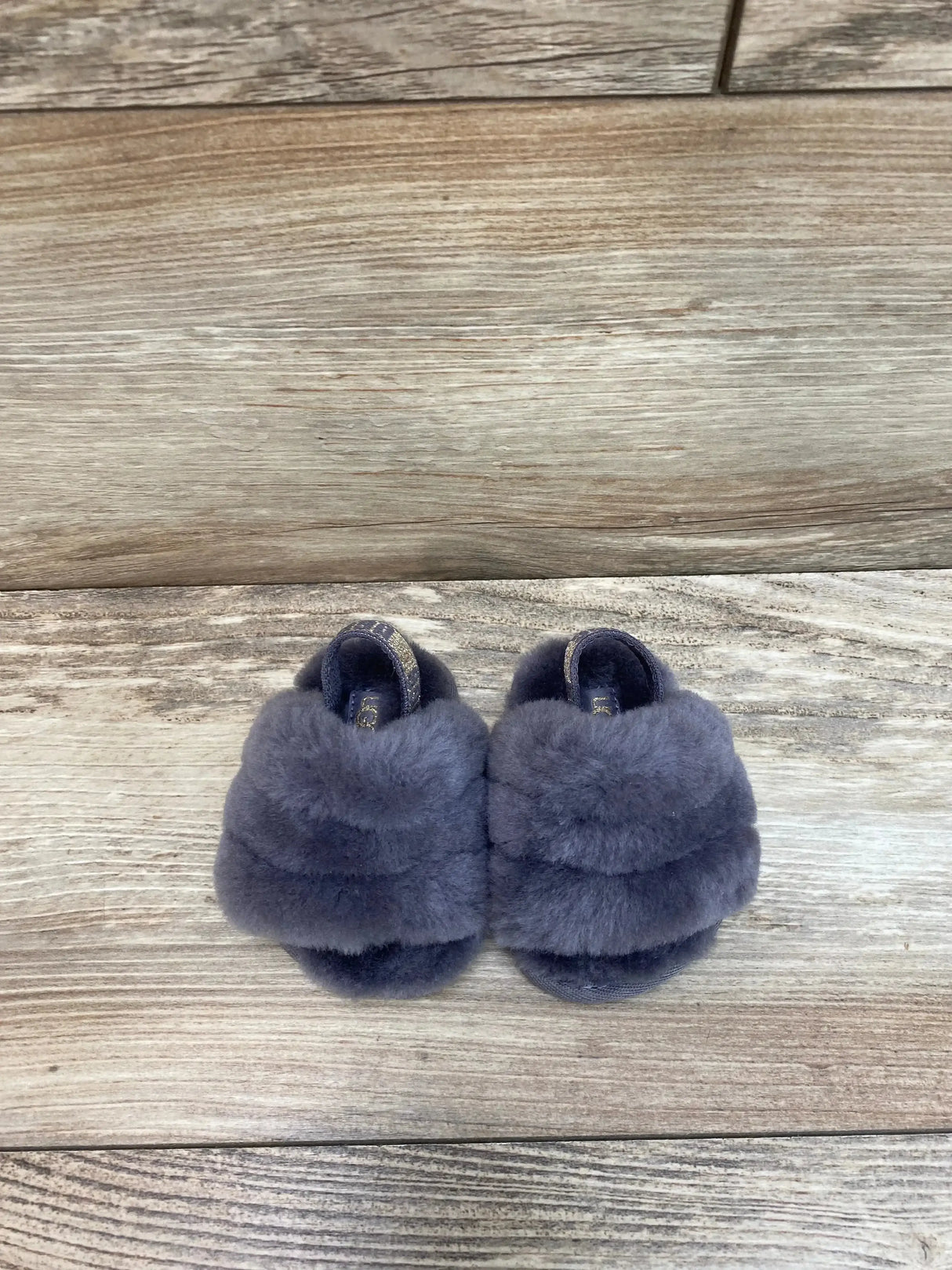 Top view of UGG Fluff Yeah Slides in grey sz 2c/3c showcasing plush fuzzy upper bands and elastic back strap with wood plank background